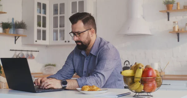 Man working on his laptop in the kitchen — Stock Photo, Image