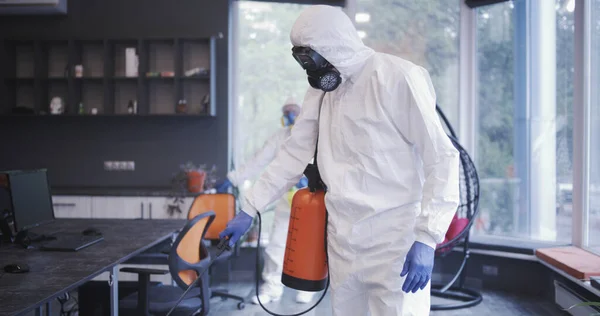 Hombres con trajes de materiales peligrosos desinfectando la oficina —  Fotos de Stock