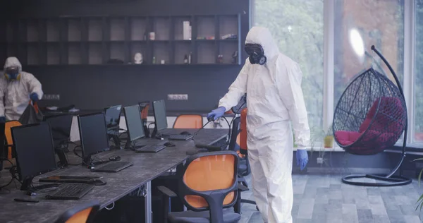 Hombres con trajes de materiales peligrosos desinfectando la oficina — Foto de Stock