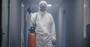 Tehlikeli madde giysileri içindeki adamlar binayı dezenfekte ediyor.