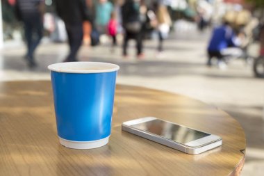 Tek kullanımlık kahve fincanının yanındaki akıllı telefon.