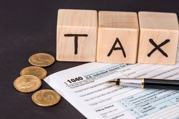 1040 tax form, wooden cubes tax pen and coin on black