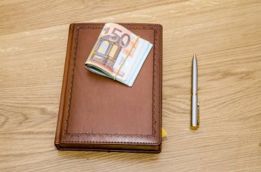Kahverengi lüks notepad ile topu kalem ve bazı Avrupa Lirası ahşap masa üstünde kapalı
