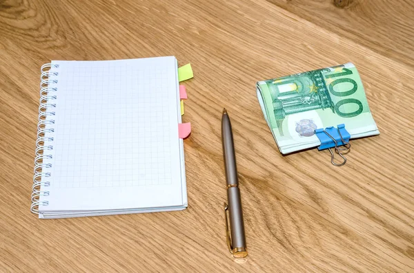 open daily planner with ball pen, one hundred euro banknotes on wooden table background