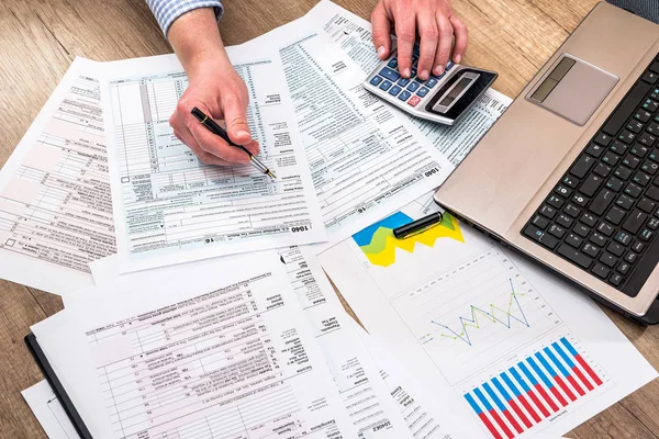 man filling tax form with business report, chart, laptop