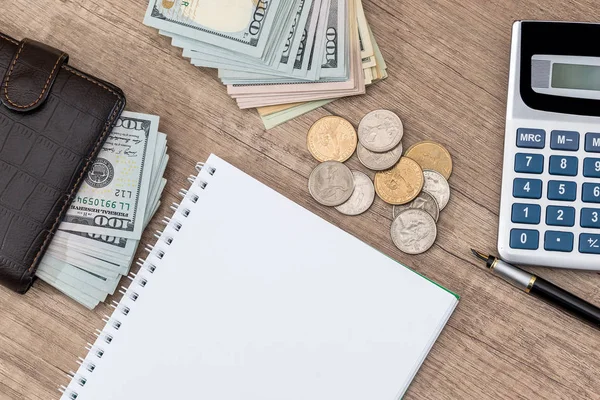 notepad with pen, calculator, dollar bills on desk.