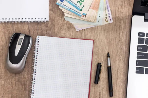 laptop, pen, euro banknote and notepad on desk.