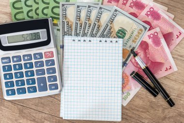 100 dolar, euro ve yuan faturaları not defteri ve hesap makinesi ve kalem üstünde okul sırası ile.