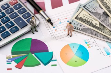 Dolar, hesap makinesi ve küçük oyuncak insanlar finansal grafiklerle