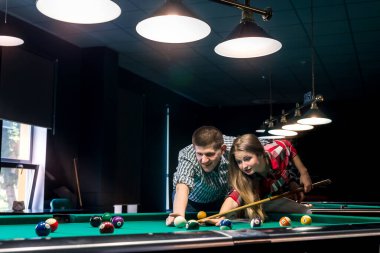Erkek, kız arkadaşına bilardo öğretiyor. Barda bir çift.