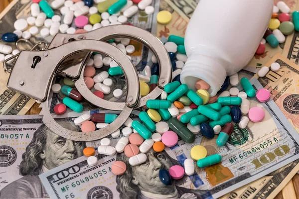 Dispersed pills from container with handcuffs on dollar banknotes