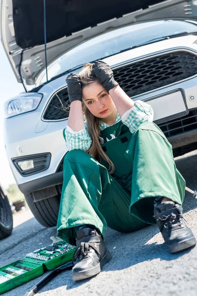 Exhausted woman mechanic with broken car on roadside