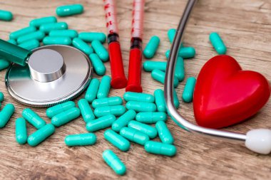 Stetoskop, haplar, oyuncak kalp ve şırınga masanın üstünde.