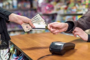 Kadın eli, ödeme olarak kasiyere dolar ve kart veriyor.