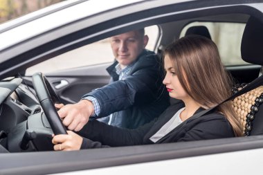 Instructor helping young woman drive a car