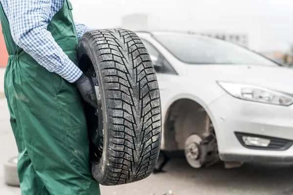 Arbeiter hält Reserverad an kaputtem Auto fest — Stockfoto