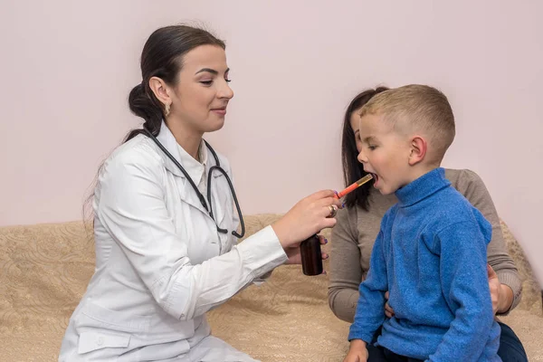 Kinderarts geeft medicijnen aan kleine jongen zittend op moeder knieën — Stockfoto