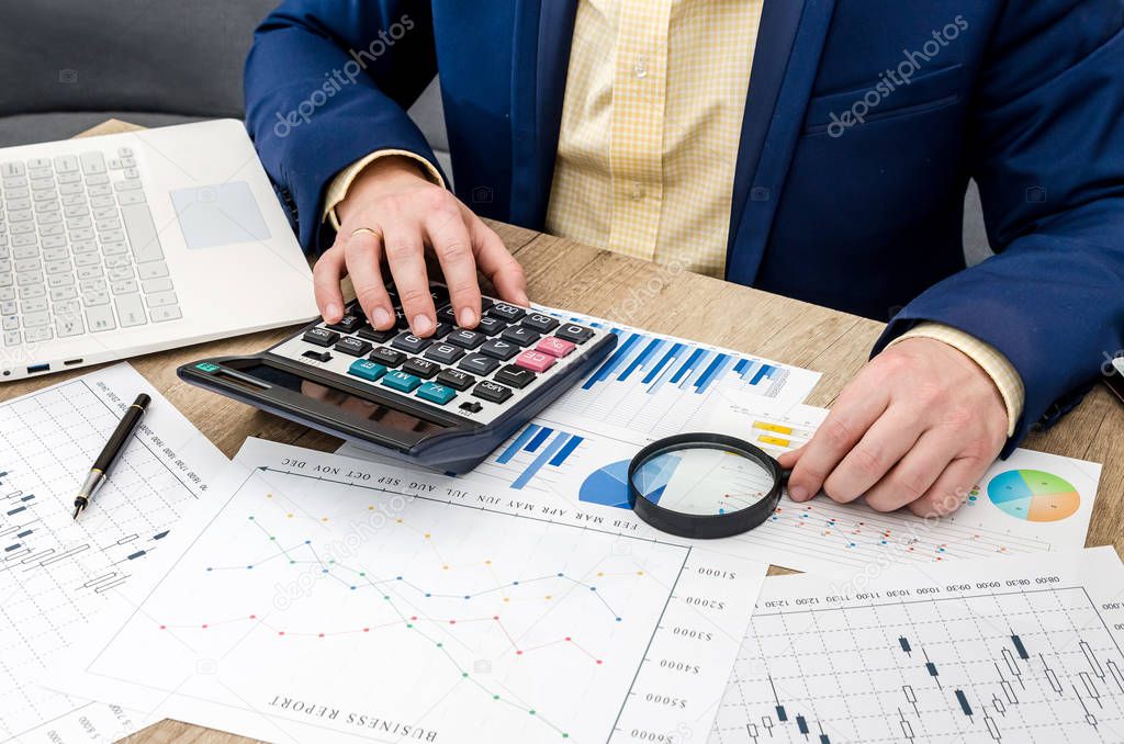 Businessman analyzing business graphs with magnifying glass