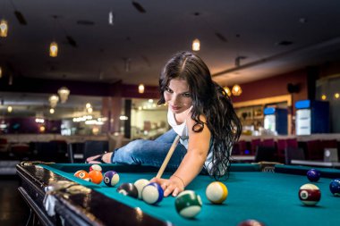 Esmer adam masada oturmuş bilardo oynuyor.