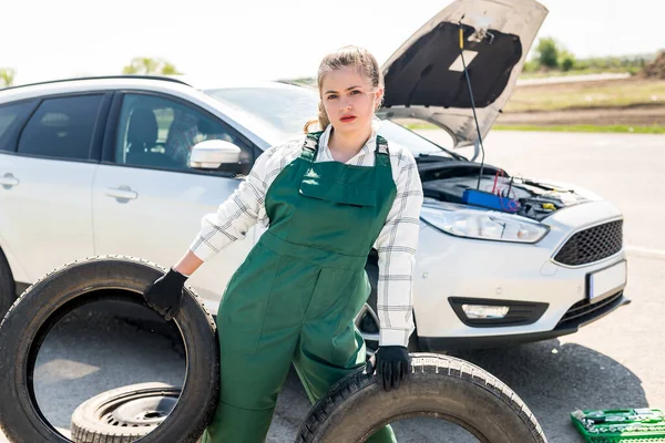 Mechanic posing with tyres on roadside with car