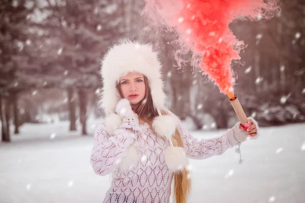 Kış parkında elinde kırmızı duman bombası olan bir kadın.