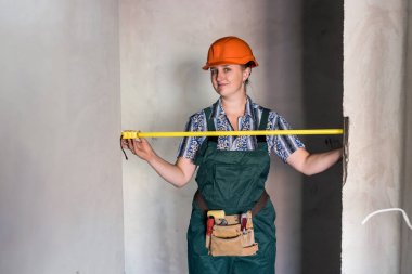 Kasklı ve koruyucu üniformalı bir kadın taksimetreyle poz veriyor.