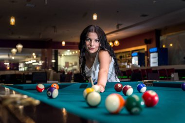 Güzel esmer kadın barda bilardo oynuyor.
