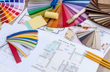Masanın üzerinde ev planı vardı, renkli ve ahşap tasarımlar, iş aletleri.
