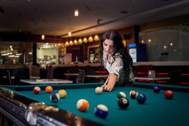 Güzel esmer kadın barda bilardo oynuyor.