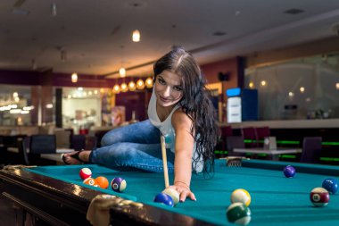 Esmer adam masada oturmuş bilardo oynuyor.