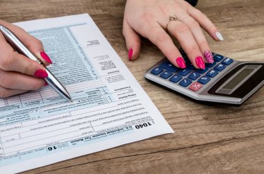 İş kadını 1040 formu ve hesap makinesiyle çalışıyor.