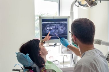 Doktor dişçi hastanın röntgenini gösteriyor.