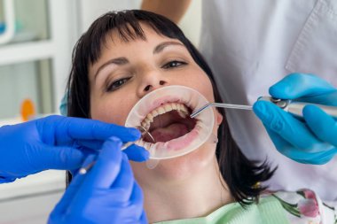 Dentist's and assistant's hands with tools and patient on chair