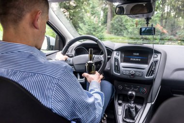 Şoför elinde direksiyon ve bir şişe alkol içeceği tutuyor.