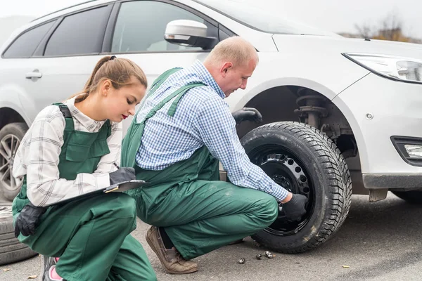 Mujer inspeccionando cómo mecánico de fijación de la rueda del coche —  Fotos de Stock