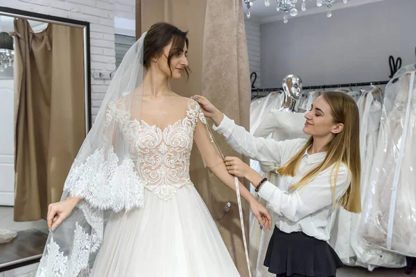 Tailor measuring wedding dress on bride in store