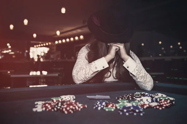 Woman in casino closing face with hands and hat