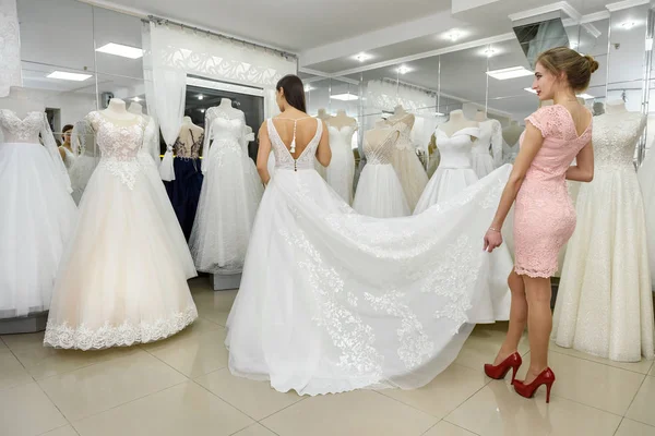 Assistente negozio aiuta sposa con abito da sposa in boutique — Foto Stock