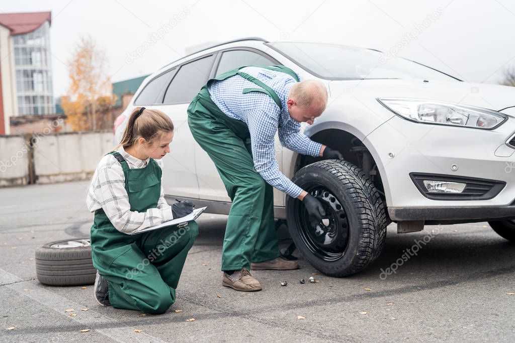 Woman checking how worker changing wheel of a car 