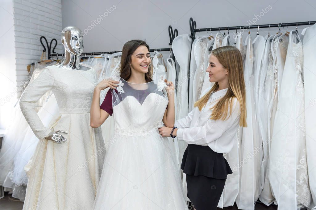 Tailor in wedding salon helping bride to try on  dress
