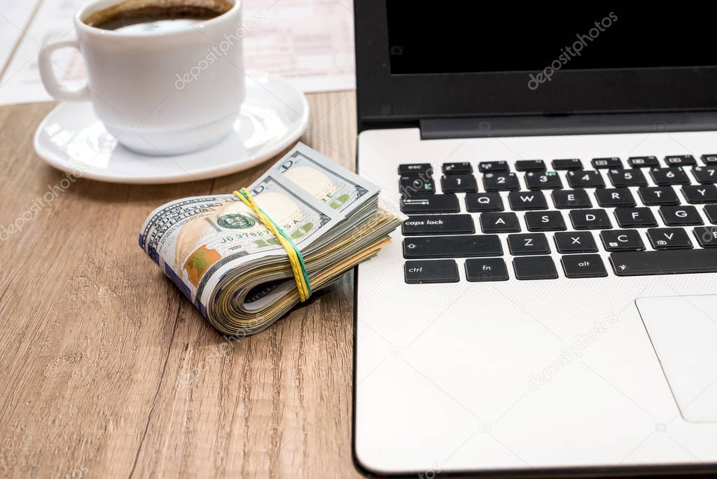stack of dollar, cup of coffee and laptop on desk