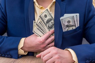 Businessman hiding dollars into pocket in jacket