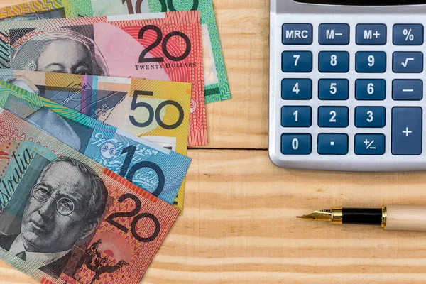 Australian dollars, pen and calculator on wooden background