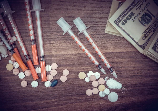 Injection syringe with cocaine pile and pills and dollar money.