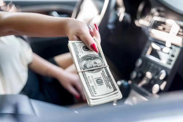 Female hands with dollar bunch inside car, closeup
