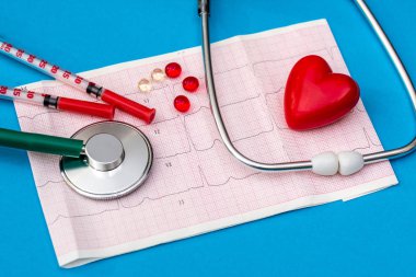 Stetoskop kardiyogram, tabletler ve mavi arka planda şırınga.