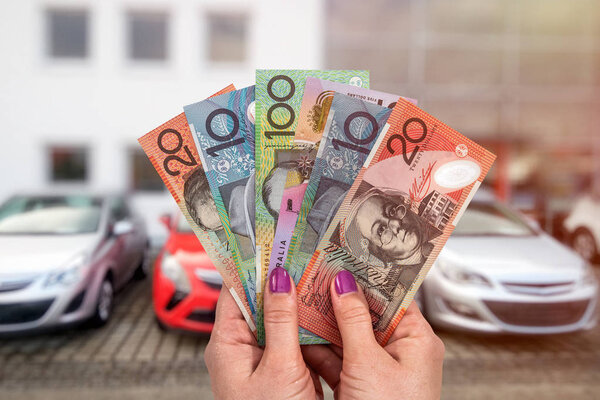 Australian dollar in hands on background of new cars