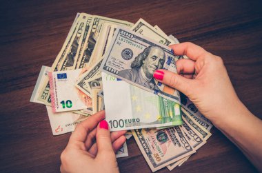 Avro ve dolar banknotlarını ahşap masanın üzerinde tutan kadın.