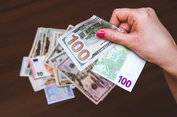 木製のテーブルの上にユーロとドルの紙幣を持っている女性 — ストック写真