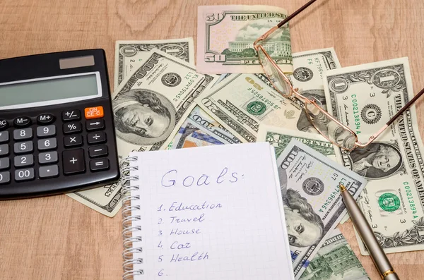 Financial goal concept, word on notepad with dollar bills, glasses and calculator